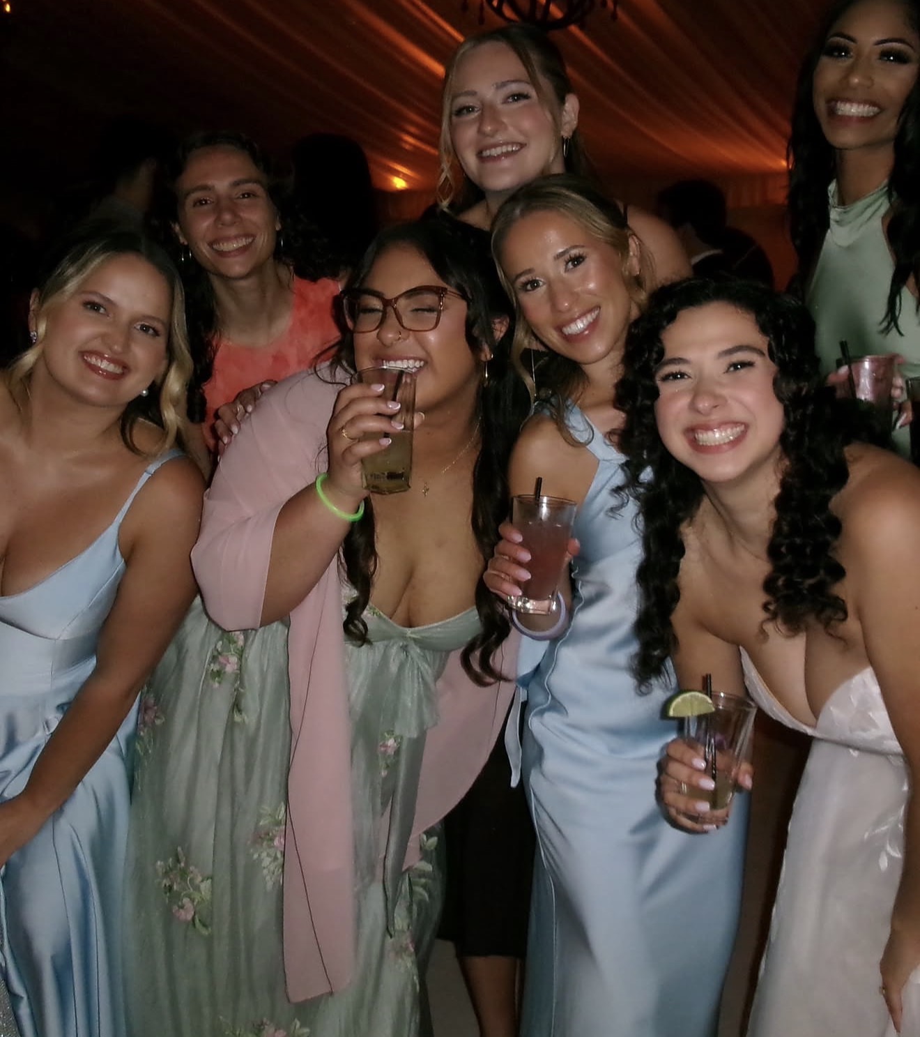 Layza and her bridesmaids laughing with drinks under the tent lights