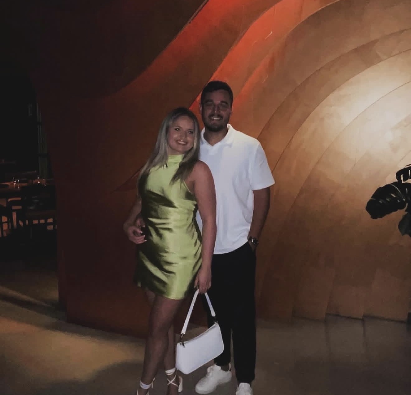 The couple dressed up against a warm sculpted wall at dinner