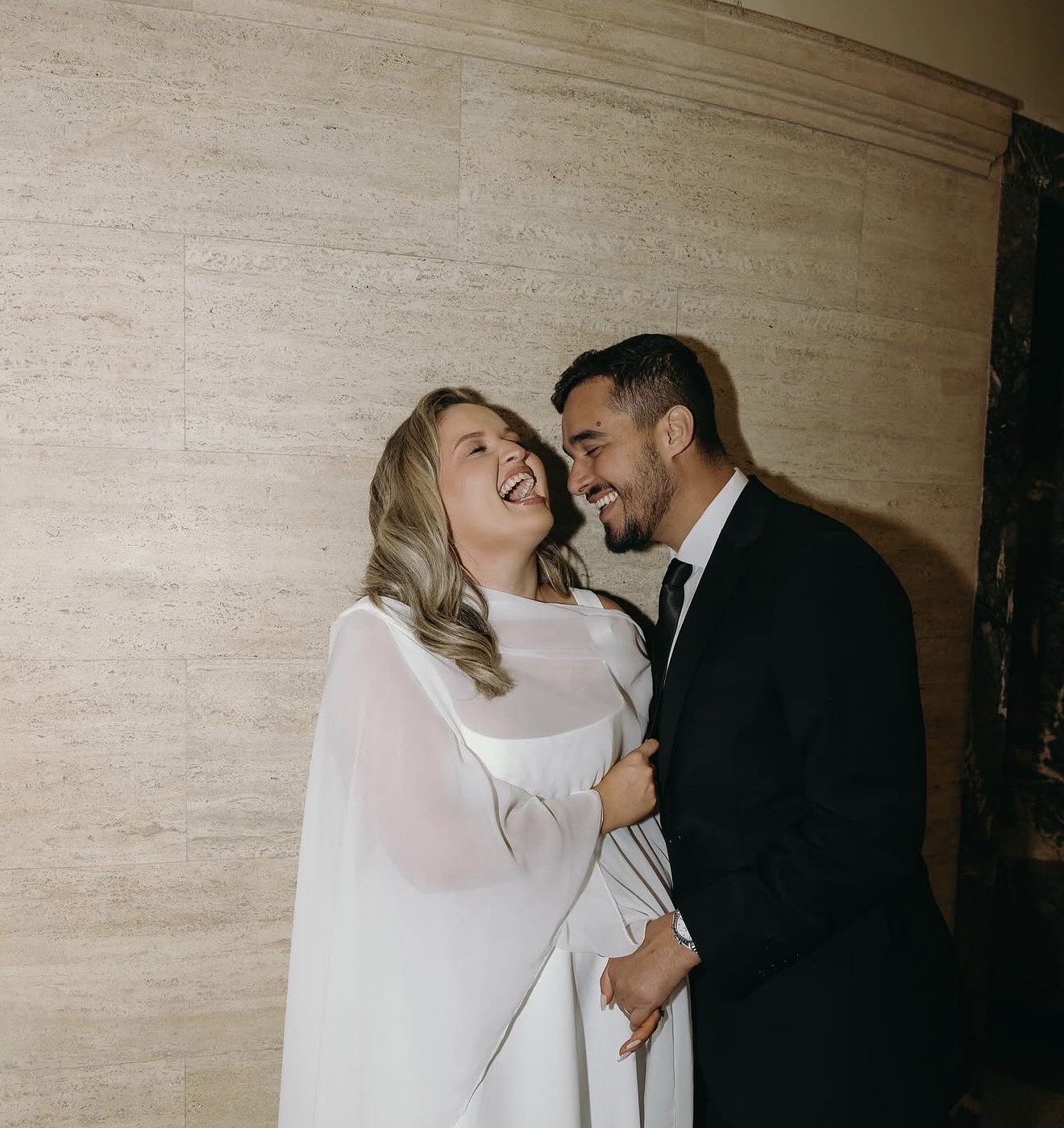 The couple laughing together against a travertine wall